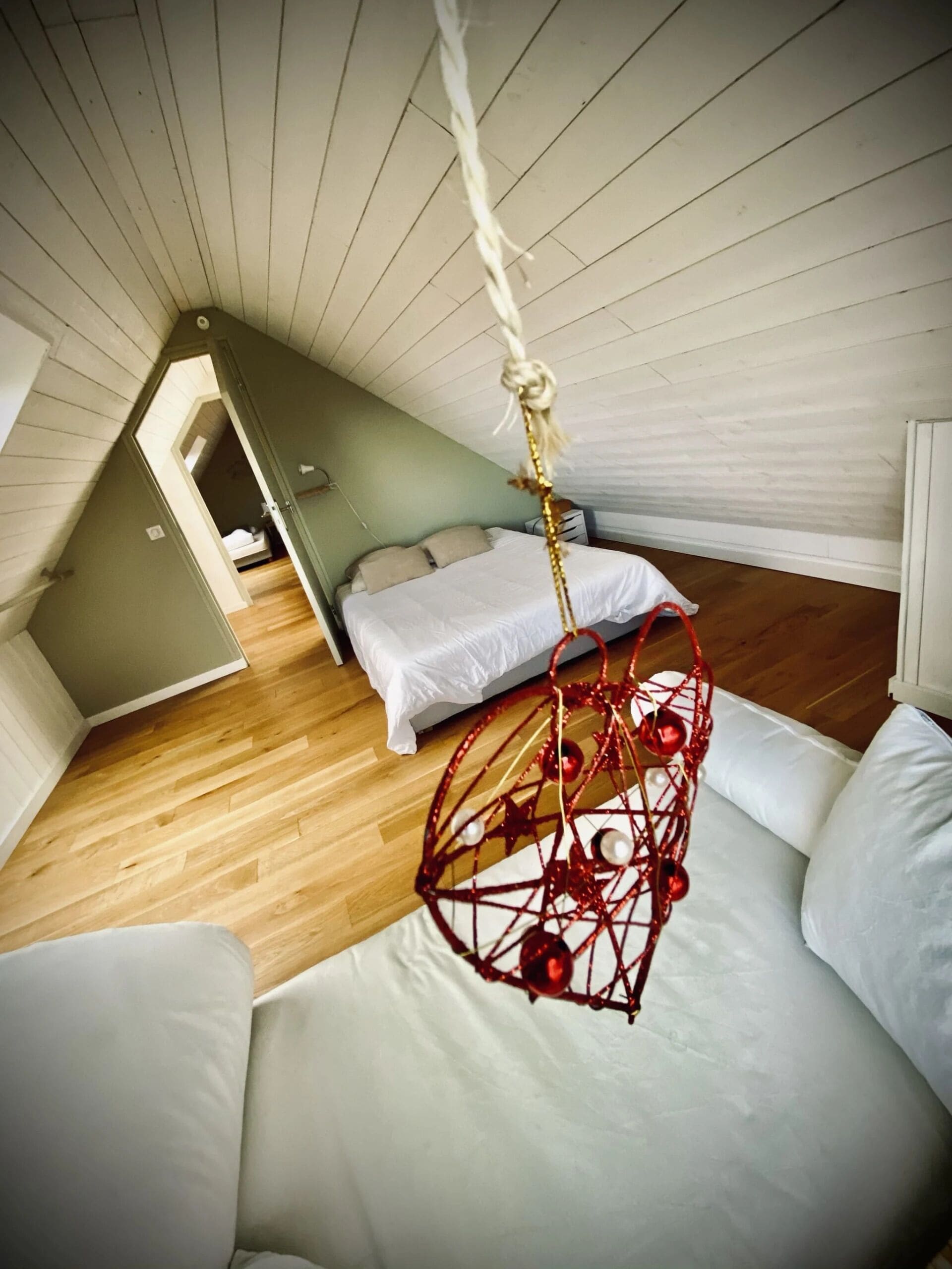 Un dormitorio con techo inclinado, una cama con ropa de cama blanca y un adorno rojo colgante.