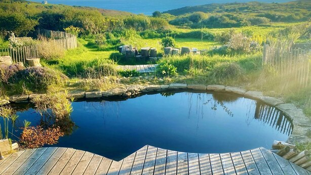 A wooden deck with two striped beach chairs overlooking a pond and a scenic view of the ocean and hills. - EMBRUNS D'HERBE SLOW CAMP (Plogoff)