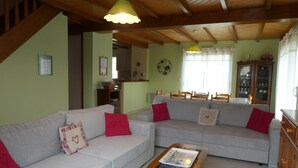 A living room with two grey sofas, red cushions, a wooden coffee table, and a kitchen in the background.