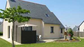 A single-story house with a sloped roof, a fenced backyard, and a small patio area with a table and chairs.