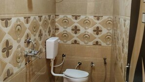 A small bathroom with a toilet, a sink, a shower, and a toilet paper holder. - Hotel The NV Grand Palace Vrindavan (Vrindavan)