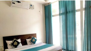 Ein Hotelzimmer mit Bett, einem Vorhangfenster, einer Klimaanlage und Holzboden.