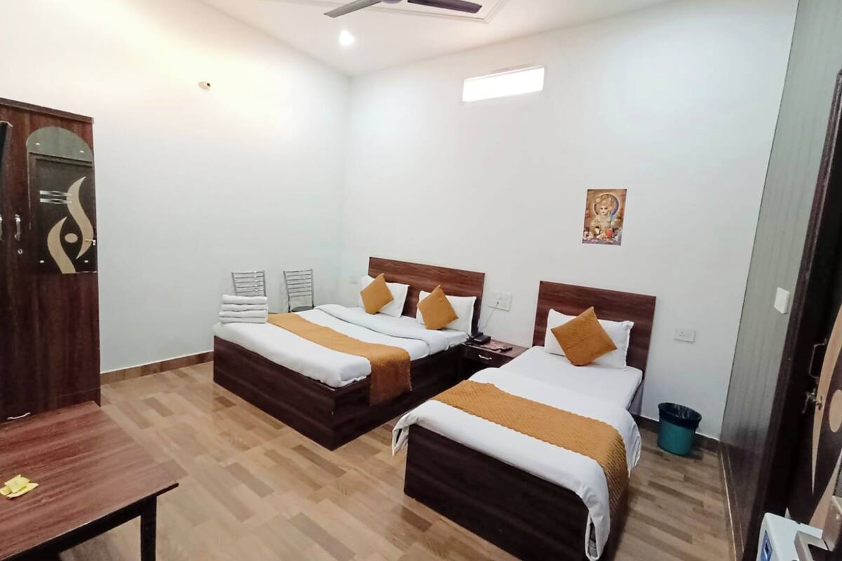 A hotel room with two beds, a wooden desk, a ceiling fan, and a small wall-mounted religious figure.