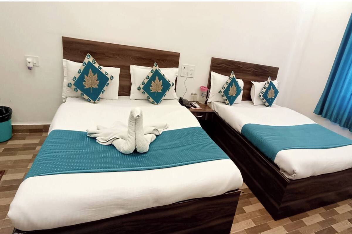 A hotel room with two beds, each with a wooden headboard, white bedding, and teal throw blankets. There is a trash bin and a small table with a phone and a pink bottle.
