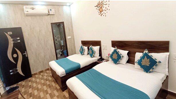 A hotel room with two beds, each with a blue blanket and decorative pillows. There is a wooden headboard, a bedside table with a phone, and a wall-mounted air conditioner. - Hotel The NV Grand Palace Vrindavan (Vrindavan)