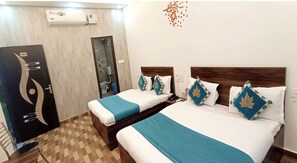 Habitación de hotel con dos camas, cada una con una manta azul y almohadas decorativas. Se observa un cabecero de madera, una mesita de noche con un teléfono y un aire acondicionado de pared.
