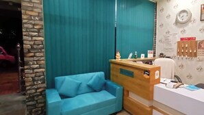 A reception area with a wooden desk, a blue sofa, and a stone wall. - Hotel The NV Grand Palace Vrindavan (Vrindavan)