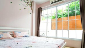 A bedroom with a large window, a bed with a floral bedspread, and a wall decal of a tree. - Canary Pool Villa Bangsaen (Chonburi)