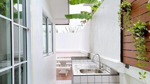 A narrow kitchen with a tiled backsplash, a sink, and a window. There are potted plants and a wooden wall on one side. - Canary Pool Villa Bangsaen (Chonburi)