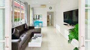 A modern living room with a leather sofa, a coffee table, a TV, and a desk with a chair. - Canary Pool Villa Bangsaen (Chonburi)
