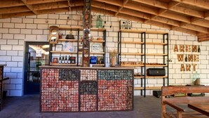 A rustic interior with exposed wooden beams, a brick wall, and shelves displaying wine and art. - Areni Wine Art (Areni)