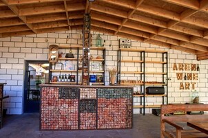 Un interior rústico con vigas de madera a la vista, pared de ladrillo y estanterías que exhiben vino y obras de arte.