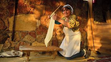 A person kneeling on a mat, rolling dough on a wooden board in a rustic stone-walled room.
