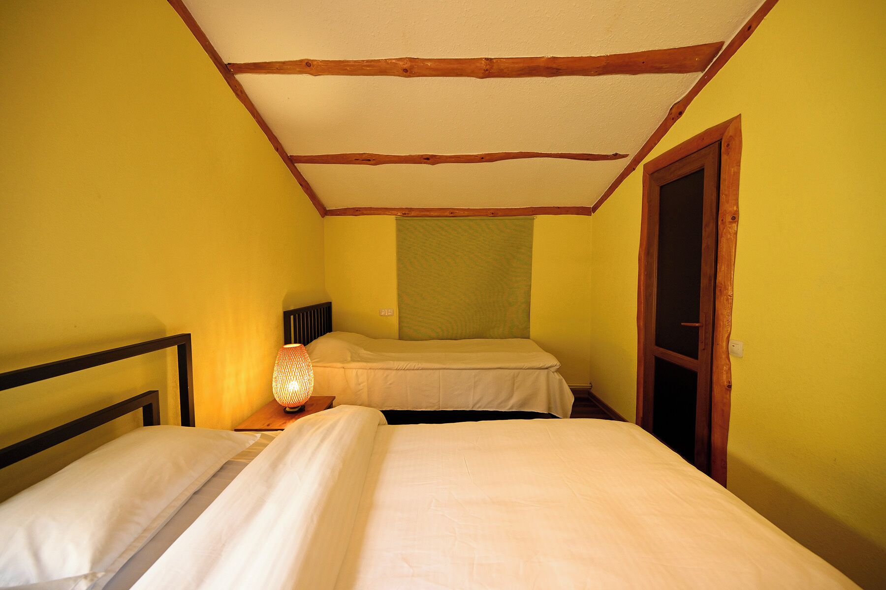 Une petite pièce avec deux lits, un plafond en bois et une porte.