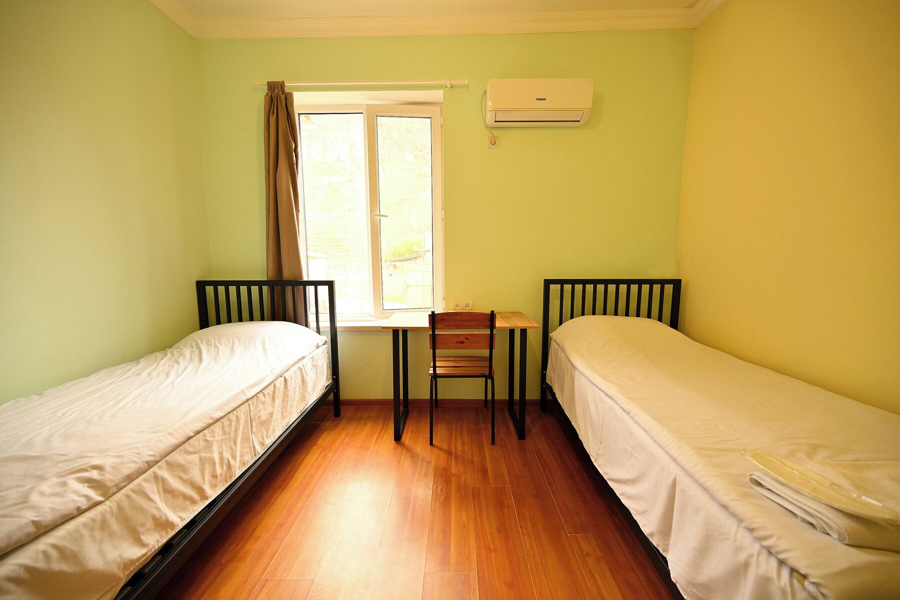 A small room with two single beds, a wooden table, and a chair.