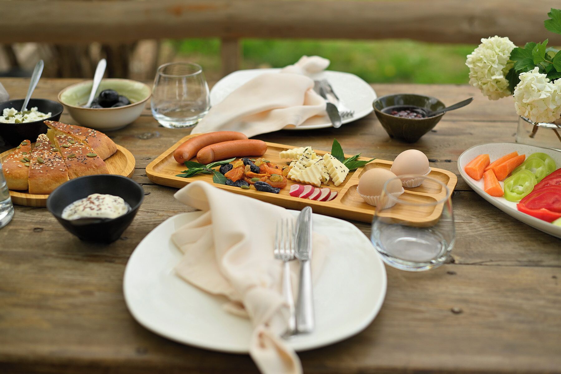 Una mesa de madera dispuesta con diversos alimentos, como pan, salchichas, huevos y verduras.