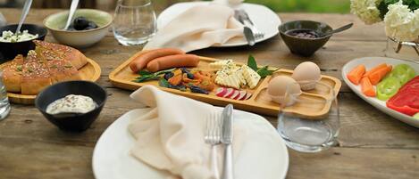 Una mesa de madera dispuesta con diversos alimentos, como pan, salchichas, huevos y verduras.