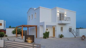 A modern villa with a white exterior, a covered outdoor seating area, and a sign indicating the name 'Villa Petalutha'.
