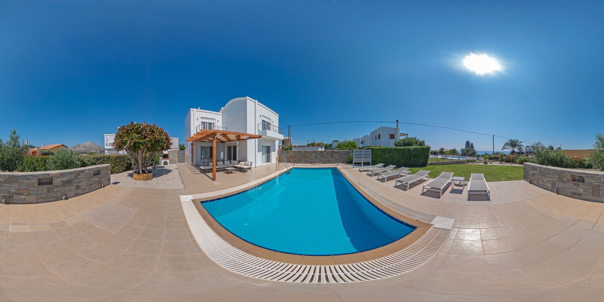 A modern pool area with a clear blue pool, sun loungers, and a stone wall.