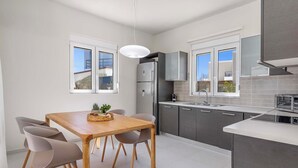 A modern kitchen with grey cabinets, a wooden dining table, and two windows.
