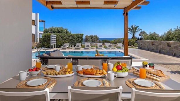 An outdoor dining area with a pool view, featuring breakfast items and a clear sky.