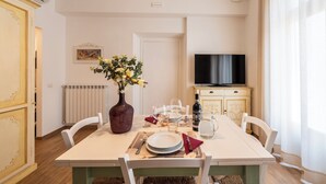 Comedor con una mesa para dos personas, un florero con flores, un televisor y un armario.