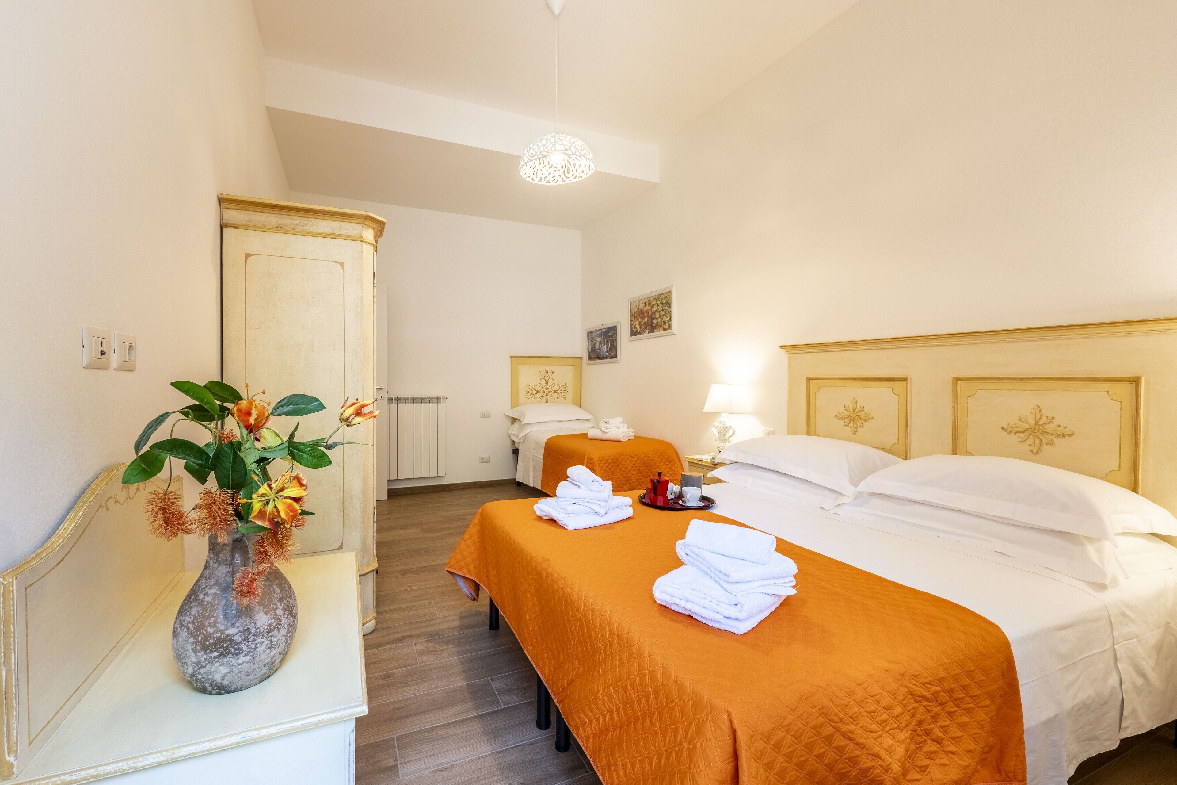 Ein Hotelzimmer mit zwei Betten, einer Blumenvase und einem Spiegel auf einer Kommode.