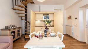Una cocina moderna con horno integrado, una mesa de comedor preparada para cuatro comensales y una escalera que sube a un nivel superior.