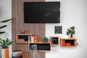 Un soggiorno moderno con TV a parete, mensole in legno con libri e oggetti decorativi, e un pannello di parete a righe.