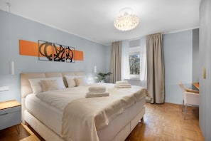 A modern bedroom with a large bed, a chandelier, and a view of the outdoors.