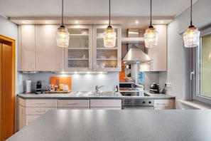 A modern kitchen with a large island, stainless steel appliances, and pendant lighting.
