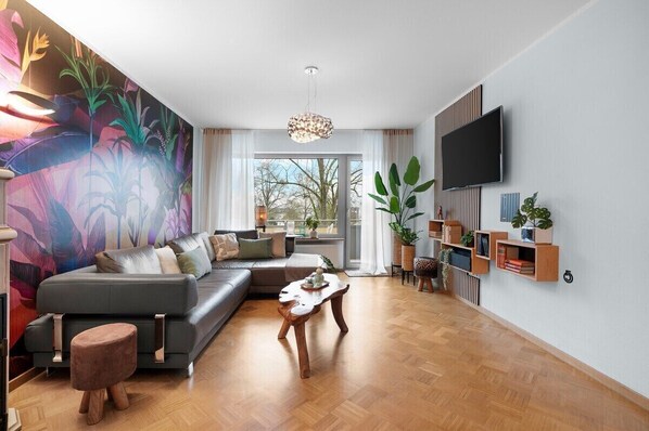A modern living room with a sectional sofa, a wooden coffee table, and a large window with a view of trees.