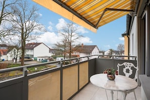 A balcony with a table and chairs, a yellow awning, and a view of the neighborhood.
