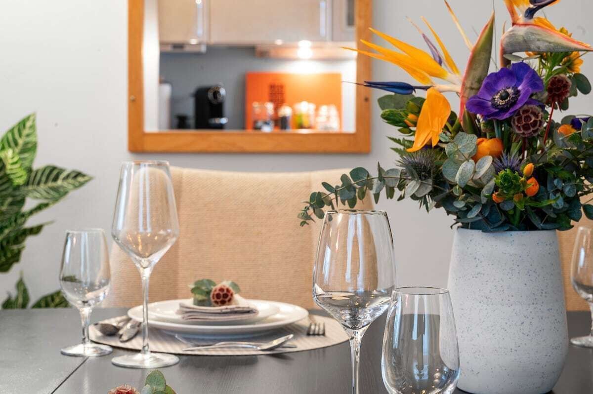 Ett matbord dukat för fyra personer, med vinglas och en blomsterdekoration i mitten.
