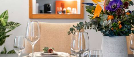 Une table à manger dressée pour quatre personnes, avec des verres à vin et un centre de table composé de fleurs.