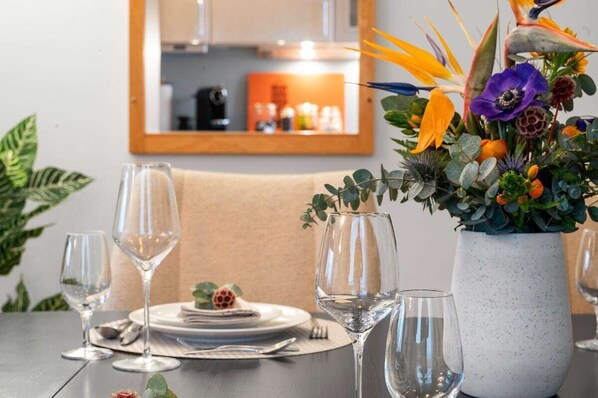 Une table à manger dressée pour quatre personnes, avec des verres à vin et un centre de table composé de fleurs.