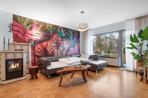 A modern living room with a fireplace, a large sofa, a coffee table, and a vibrant floral mural on the wall.