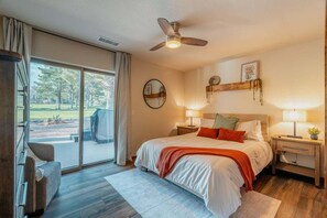 Une chambre avec un grand lit, un ventilateur de plafond, une porte-fenêtre coulissante donnant sur une terrasse et un petit bureau avec une lampe.