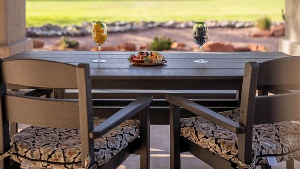 Una mesa en el patio con dos sillas, una copa de vino y un cuenco de fruta.