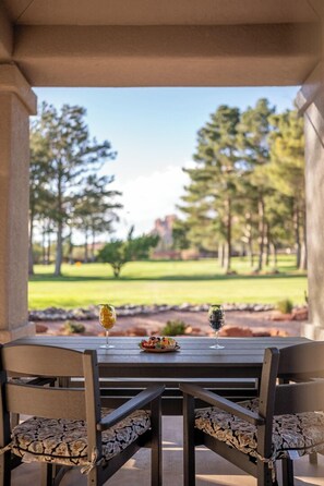 Une table de patio avec deux chaises, un verre de vin et un saladier de fruits.
