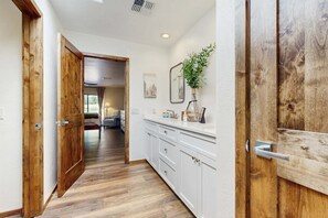 Un couloir doté d’un plancher en bois, de meubles blancs et d’une porte ornée d’un miroir et d’une plante.