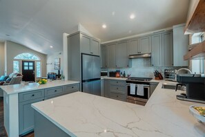 Una cocina moderna con armarios grises, una isla grande, electrodomésticos de acero inoxidable y vistas al salón.