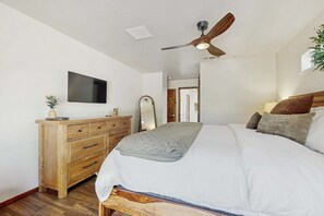 Un dormitorio con cama, cómoda de madera, ventilador de techo y televisor montado en la pared.