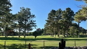 Un campo de golf con cielo despejado, árboles y una zona rocosa con valla.