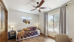 Un dormitorio con cama, mesitas de noche, ventilador de techo, ventana con cortinas y vistas al exterior.