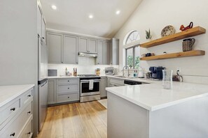 Una cocina moderna con gabinetes grises, electrodomésticos de acero inoxidable y estantes de madera.