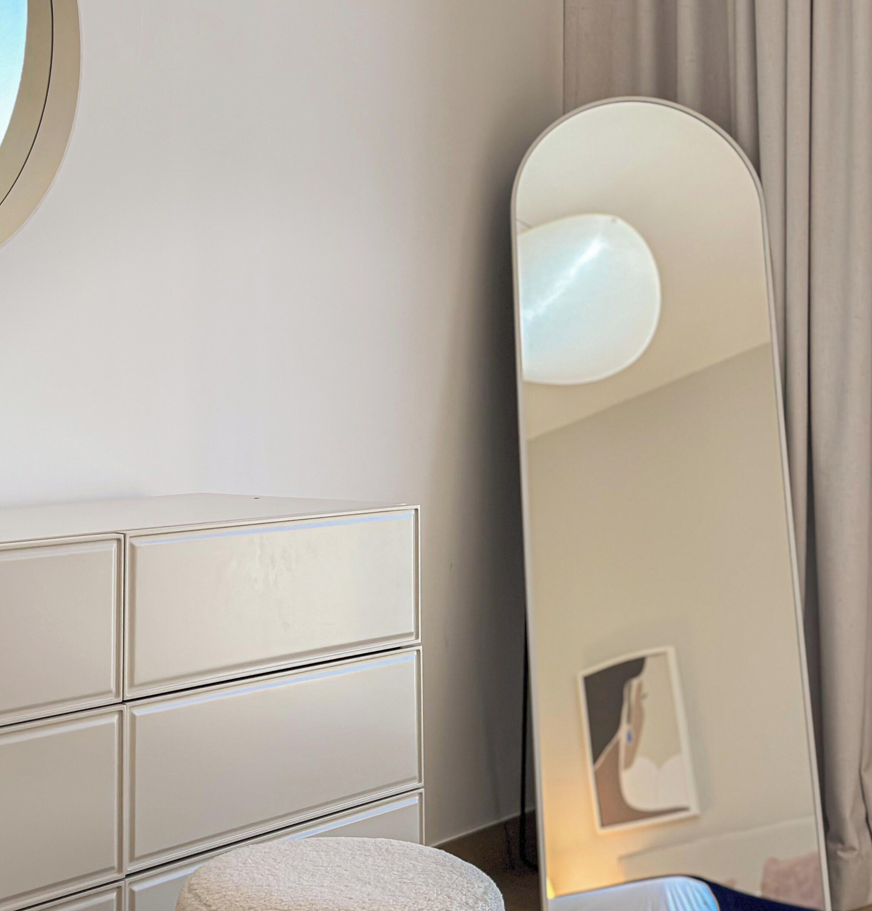 Een moderne hotelkamer met een witte dressoir, een ronde spiegel en een grote spiegel die de kamer weerspiegelt.