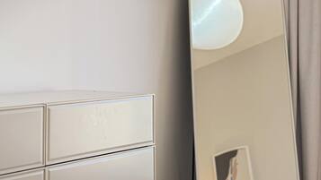 Een moderne hotelkamer met een witte dressoir, een ronde spiegel en een grote spiegel die de kamer weerspiegelt.