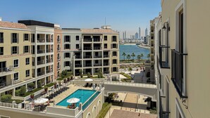 A hotel with a rooftop pool, multiple balconies, and a view of the city skyline and sea. - HiGuests - La Rive Classy 2BR & Balcony (Dubai)