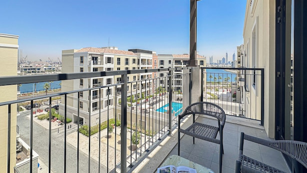 A balcony with a view of a swimming pool, buildings, and a distant city skyline. - HiGuests - La Rive Classy 2BR & Balcony (Dubai)